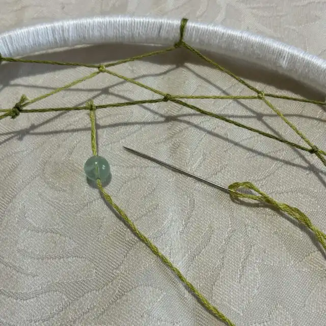 Для упрощения работы нитку продеваем в иголку и продеваем бусину. Далее все по классике — завязываем узелок на предыдущим ряду.